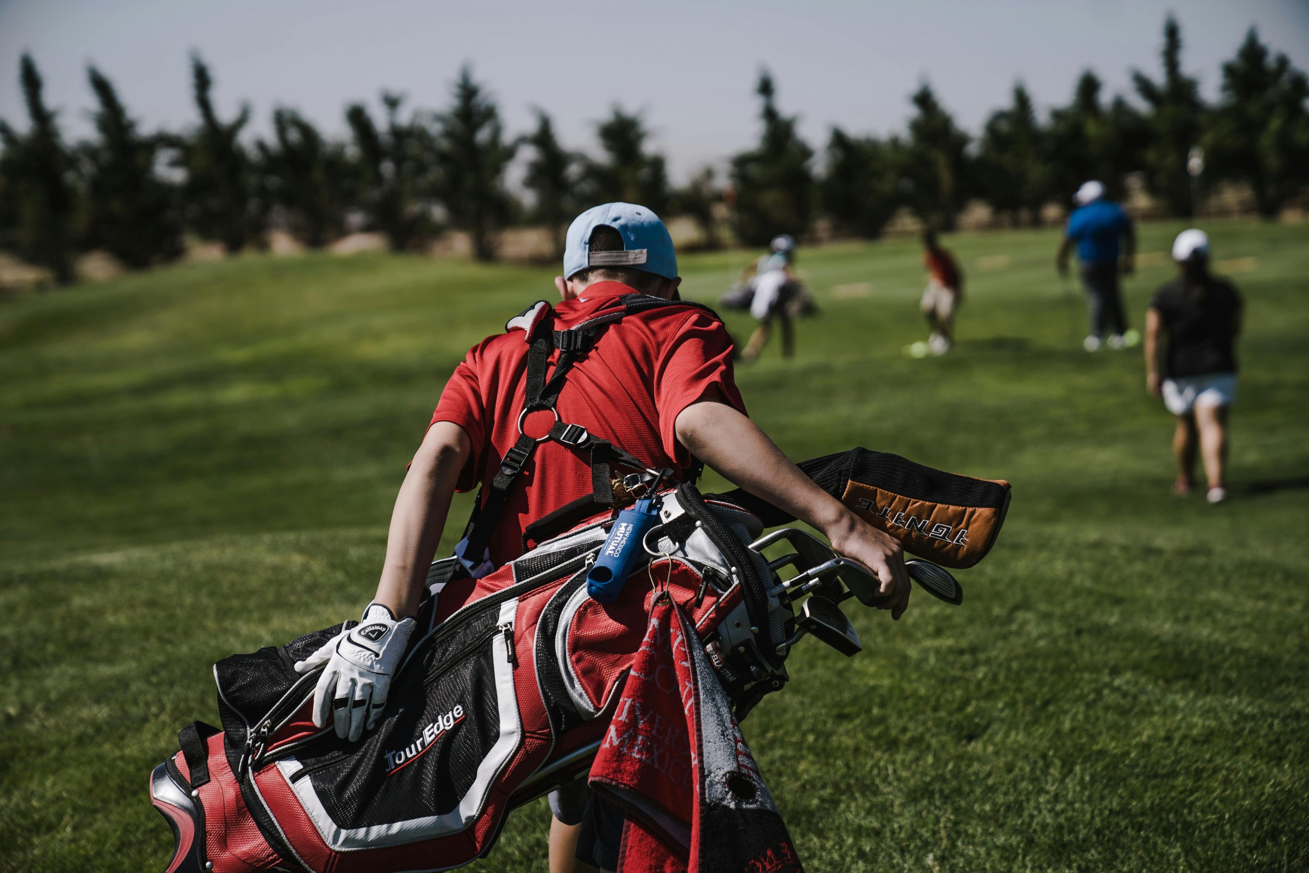 A golfer in red carrying a bag on a lush green golf course during a sunny day.