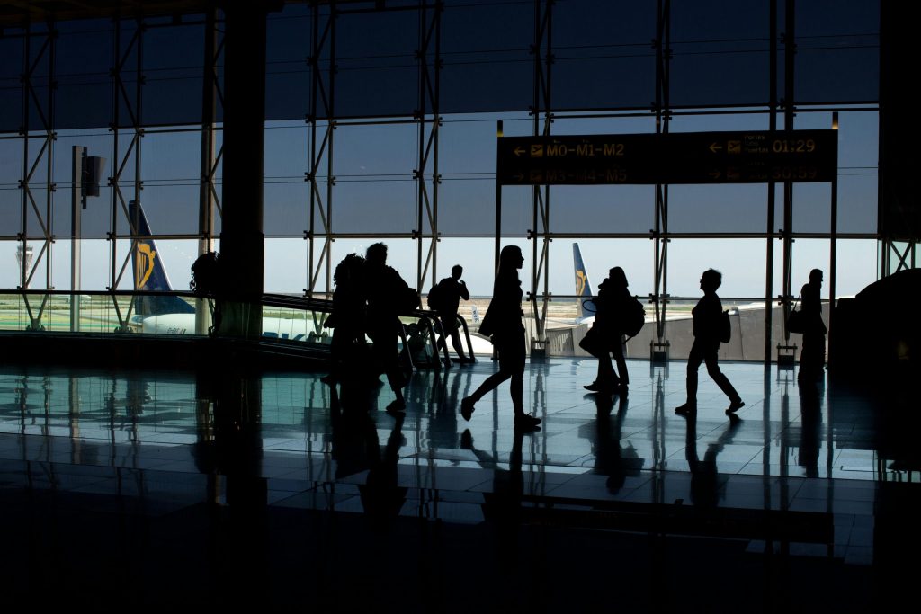 Airport Transfers 16 Silhouettes of people walking in an airport terminal, plane tail visible outside.