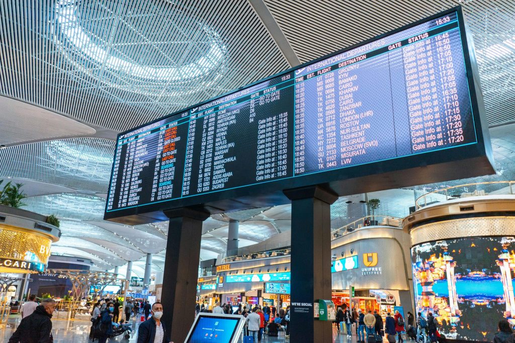 Airport Transfers 1 Passengers walk through Istanbul Airport's departure area, surrounded by stores and flight information displays.